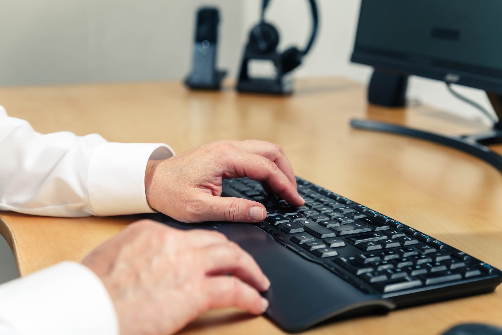 Hände an einer Tastatur, daneben Telefon und Bildschirm