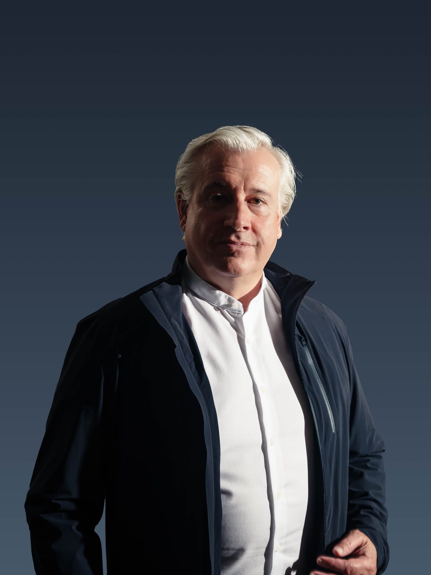 René Giloy stehend im dunklen Sakko vor dunkelblauem Hintergrund
